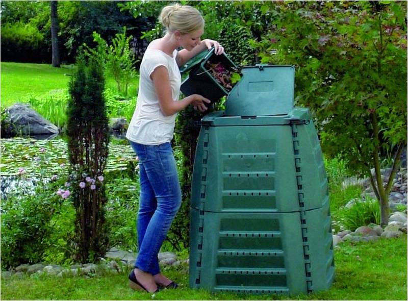 Девушка выбрасывает мусор в зеленый стационарный, пластмассовый компостер.