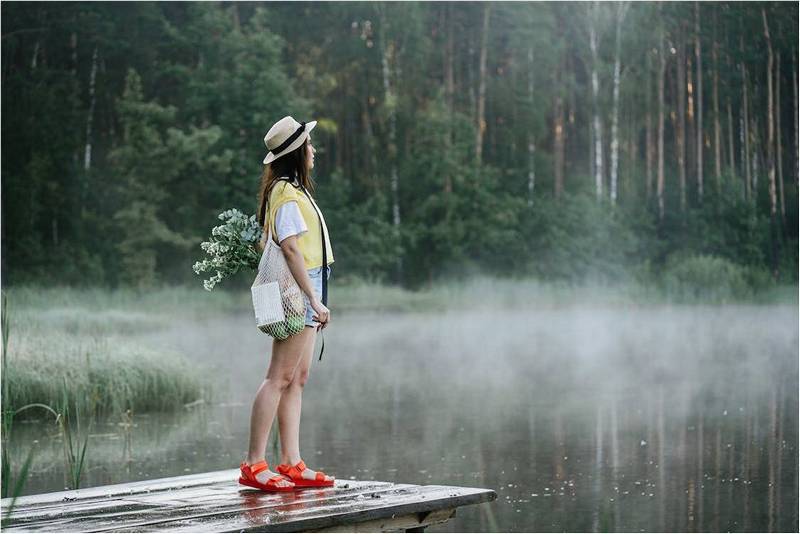 Девушка стоит у пруда, дымка над водой.