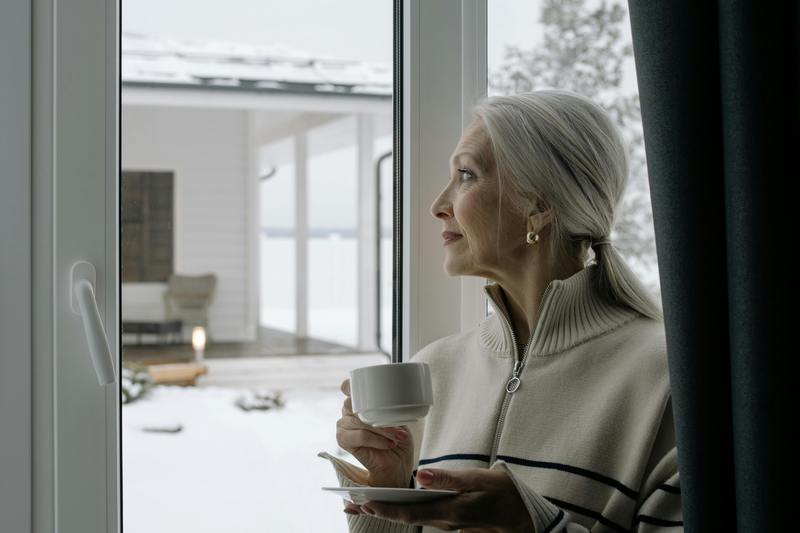 Женщина с чашкой чая смотрит в окно.